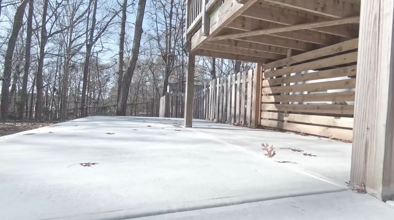 Clean concrete patio slab under a deck with wood railing in Laredo, TX